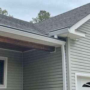 A picture of seamless gutters on a house with gray siding and a shingle roof.