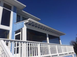 A home with blue siding and a large wrap-around porch has replacement seamless gutters.